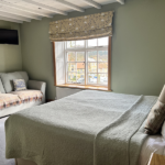 Double room with couch in pale green colours with a bright widow with floral blind