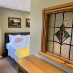 Stained glass internal window in double bedroom with double bed with yellow throw in the background