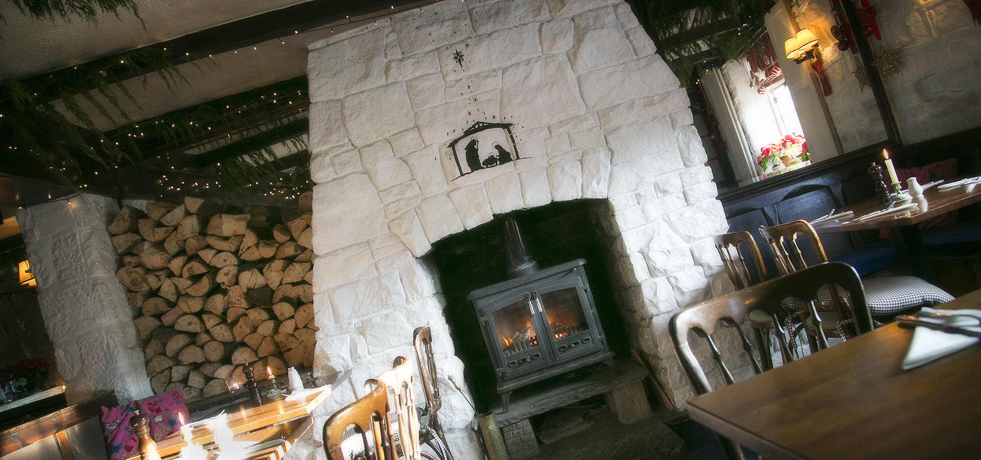 White stone fireplace with log burner, logs stored beside it and tables set for lunch