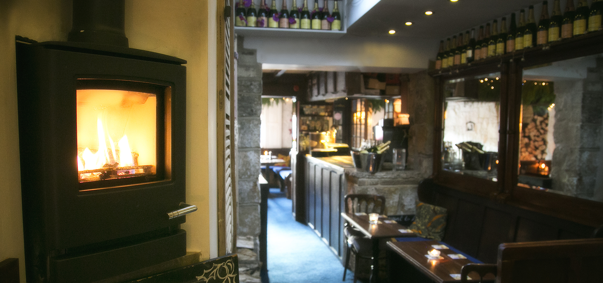 Log burner in the back restaurant area with tables set for dinner service in the background along with the bar