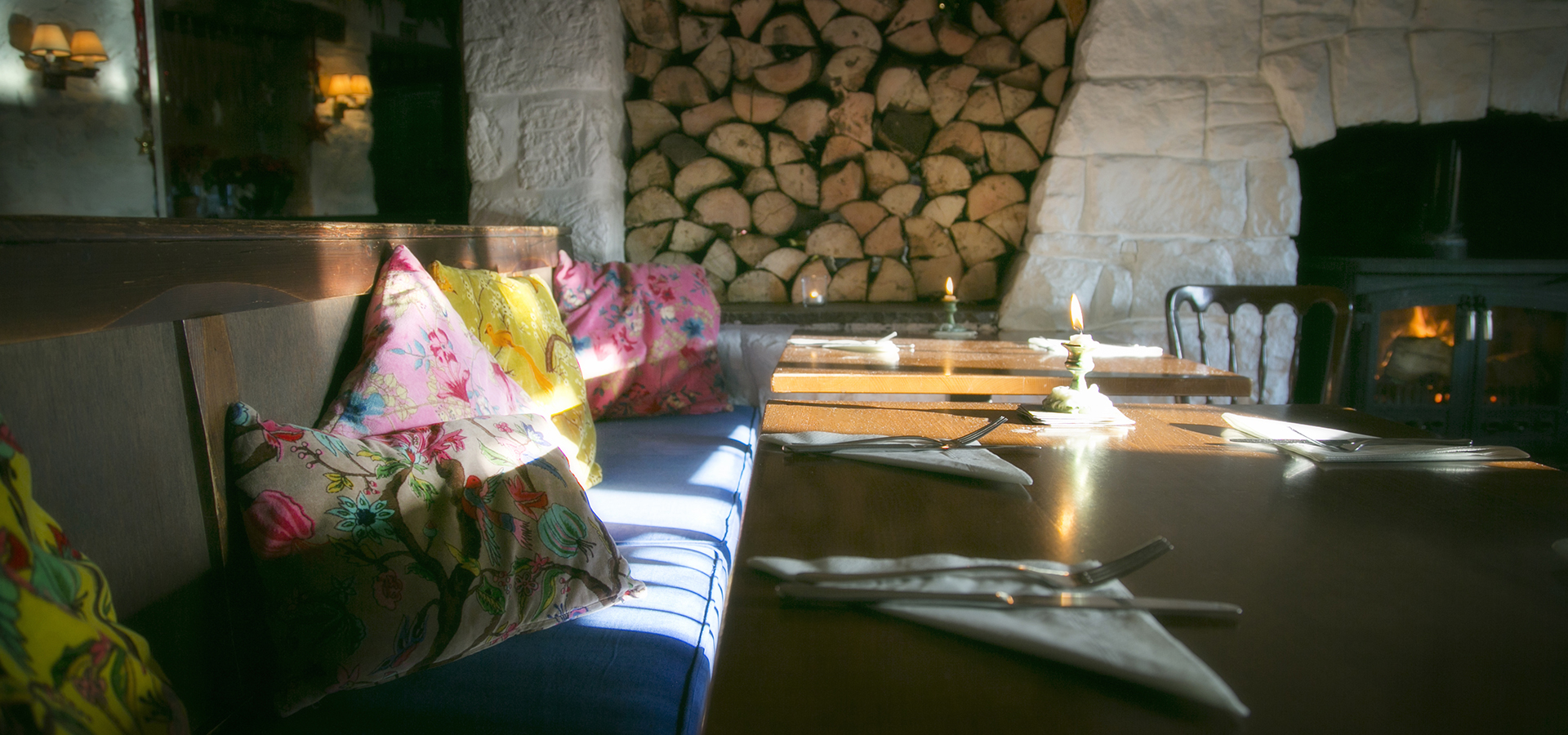Close up of a table set for dinner service with the bench seat filled with colourful cushions