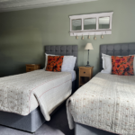 Twin guest room showing both beds covered in pale floral bedding and bright orange floral scatter cushions